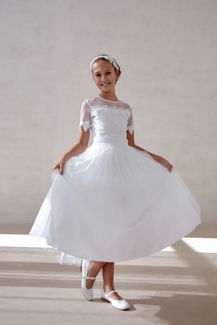 Biała sukienka do Komunii przyozdobiona gipiurowymi listkami, na modelce