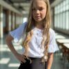 Biała bluzka z falbanami dla dziewczynki, zestawiona z czarną spódniczką. Idealna na letnie wyjścia i uroczystości.