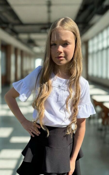 Biała bluzka z falbanami dla dziewczynki, zestawiona z czarną spódniczką. Idealna na letnie wyjścia i uroczystości.