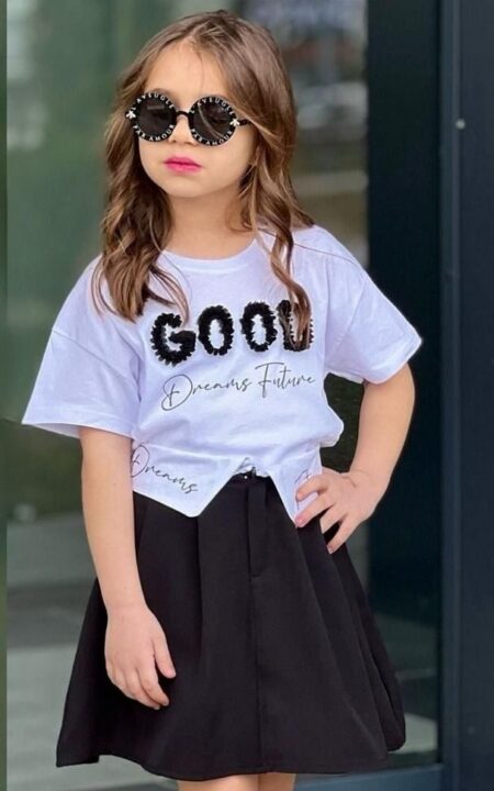 Dziewczynka w czarnej spódnicy i białej koszulce z napisem, nosząca modne okulary przeciwsłoneczne.