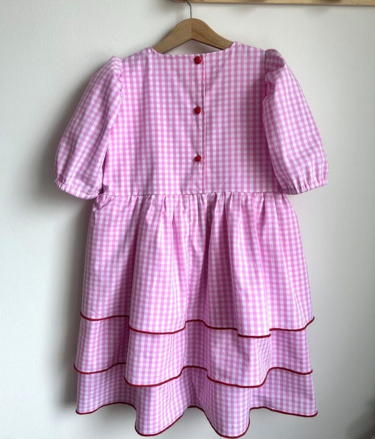 Różowa sukienka w kratkę z bufkami i czerwonymi detalami, idealna na letnie przyjęcia dla dziewczynki.