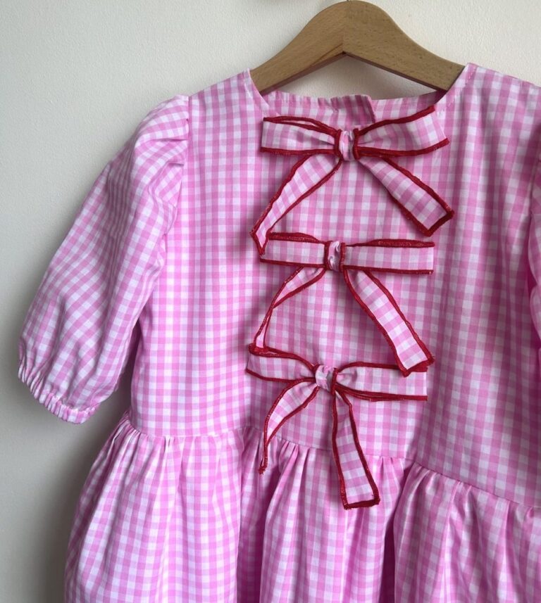 Różowa sukienka w kratkę z ozdobnymi kokardkami, idealna dla małej księżniczki.