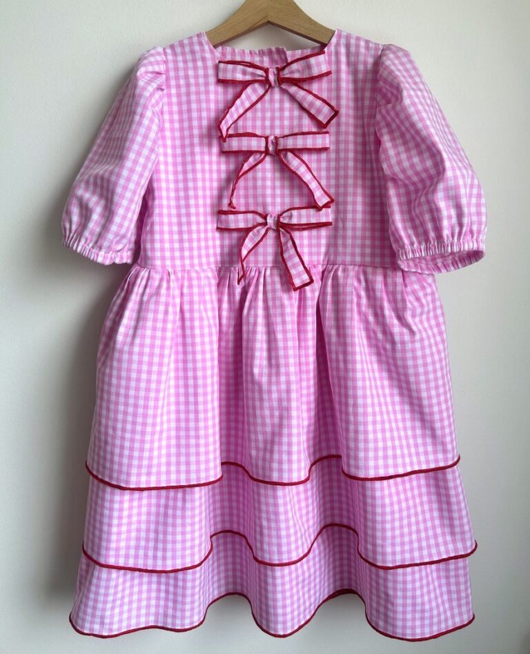 Różowa sukienka w kratkę z ozdobnymi kokardkami i falbanami, idealna na letnie przyjęcia.