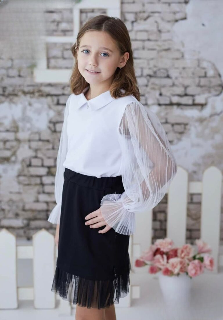 Czarna spódniczka z tiulem dla dziewczynki, idealna na eleganckie okazje, zestawiona z białą bluzką z przezroczystymi rękawami.