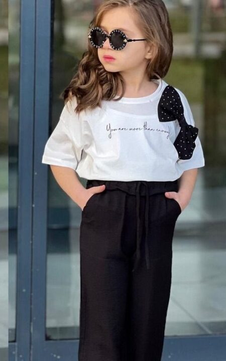 Biała bluzka z kokardą i czarnymi spodniami, idealna na codzienne stylizacje dla dziewczynki.