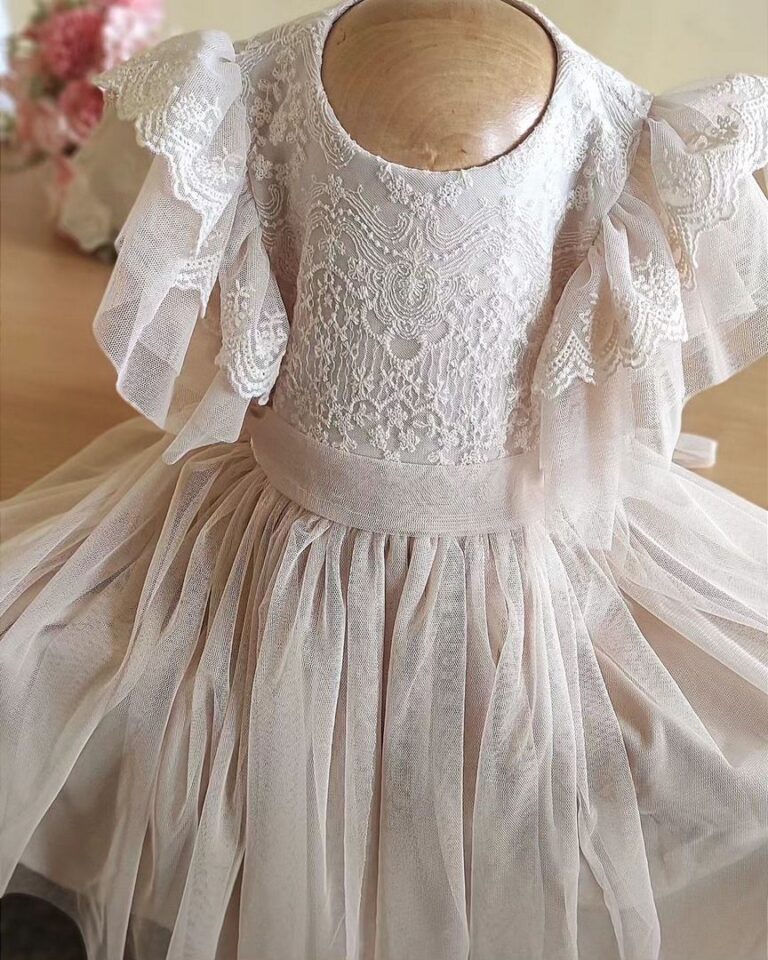 Delikatna sukienka dla dziewczynki w kolorze beżowym z koronkowymi detalami i falbanami na rękawach.