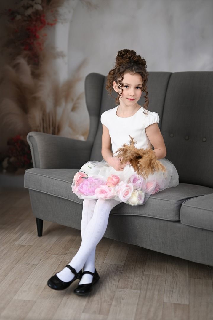 Biała sukienka dla dziewczynki z wszytymi kwiatami w dolnej części, idealna na specjalne okazje.