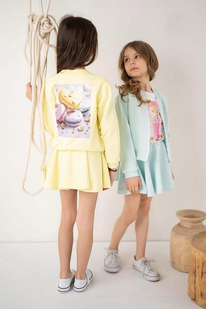 Zestaw składający się z żółtej bluzy z nadrukiem i spódnicy oraz błękitnej bluzy z nadrukiem i spódnicy, idealny na wiosenne dni dla dziewczynek.