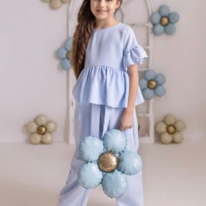 Niebieski komplet komunijny dla dziewczynki z bluzką i spodniami, trzymany w ręku bukiet w kształcie kwiatu.