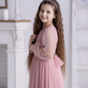 Różowa sukienka z perłami dla starszej dziewczynki z długimi, przezroczystymi rękawami i kokardą z tyłu.