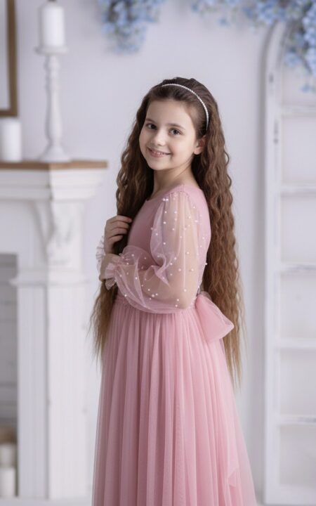 Różowa sukienka z perłami dla starszej dziewczynki z długimi, przezroczystymi rękawami i kokardą z tyłu.