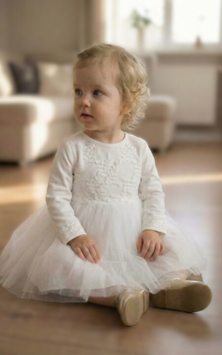 Wizytowa sukienka dla niemowlaka w kolorze białym z koronkowym wykończeniem, idealna na specjalne okazje.