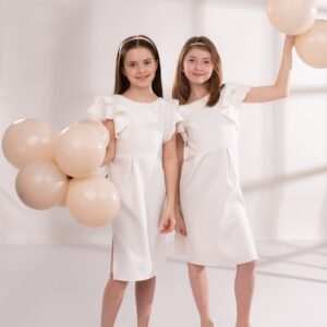 Sukienka ołówkowa w kolorze ecru z falbanami, idealna na uroczystości, noszona przez dwie dziewczynki trzymające balony.