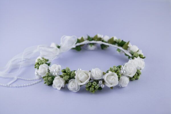 Wianek z białymi różami i zielonymi dodatkami, ozdobiony perłami i wstążką. Idealny na uroczystości i specjalne okazje.