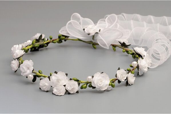 Wianek dla dziewczynki z białymi kwiatami i zielonymi liśćmi, ozdobiony białą wstążką.